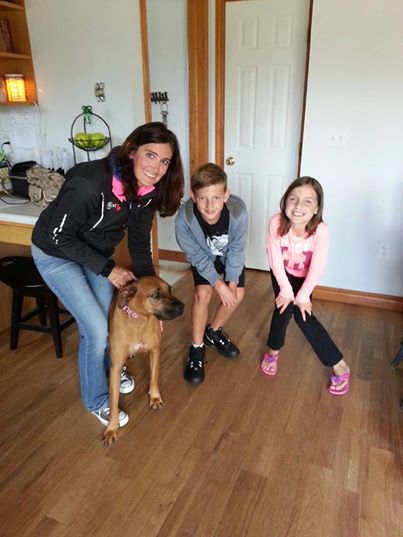 A woman and two children pose with a dog in a living room.