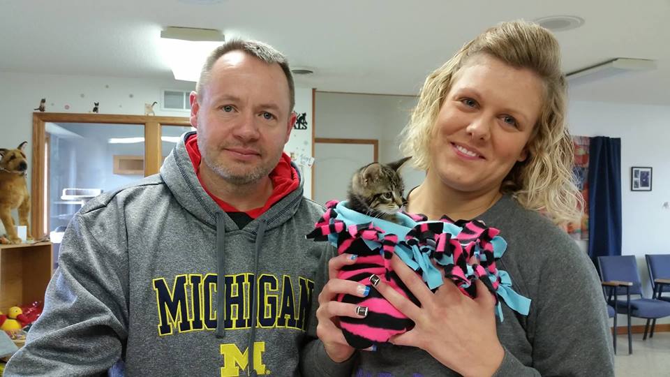 A man and woman holding a kitten in their arms.