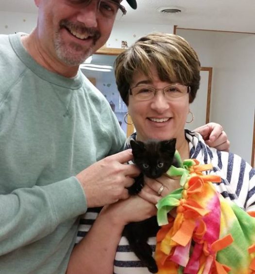 A man and woman posing with a black cat.