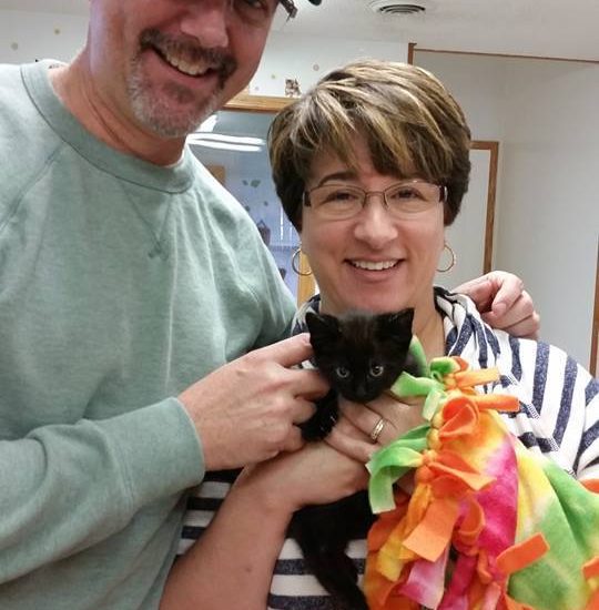 A man and woman posing with a black cat.