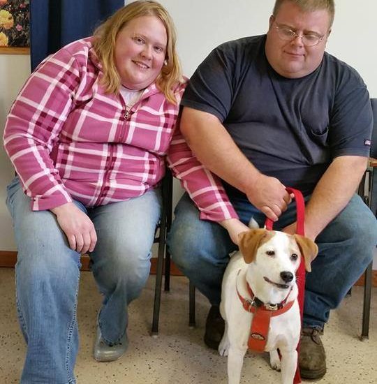 A man and woman pose for a photo with their dog.