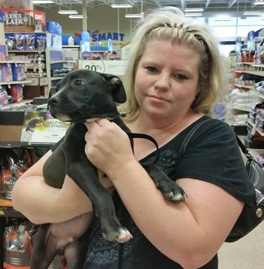 A woman holding a black dog in a store
