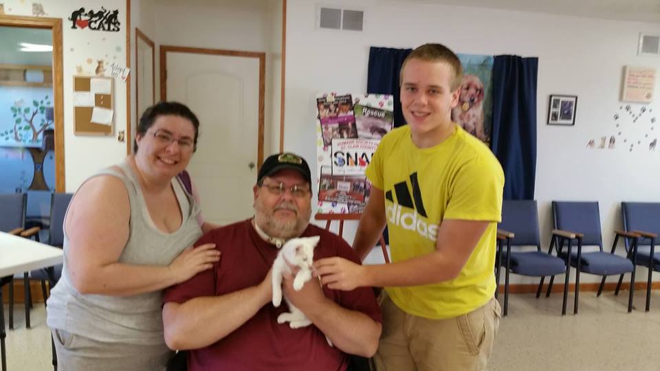 A family of three holding a white cat