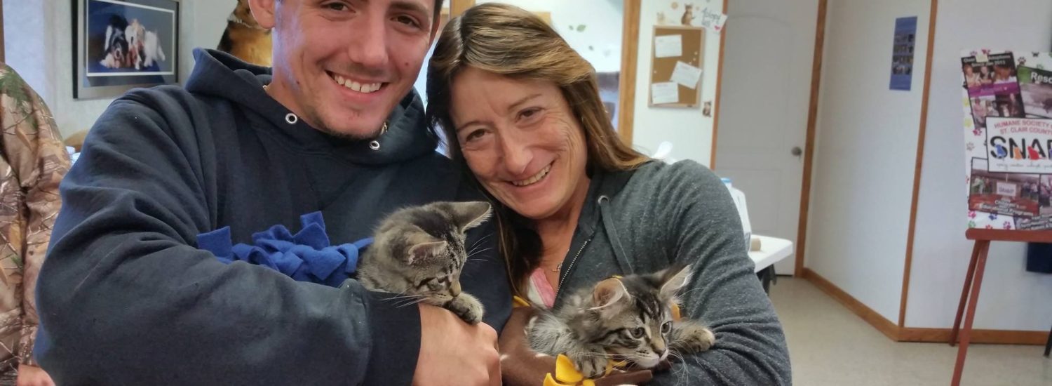 A man and woman holding kittens in a room.