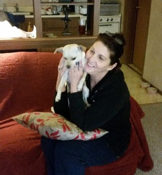 A woman sitting on a couch holding a small dog.