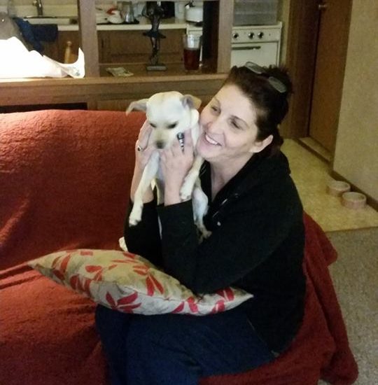 A woman sitting on a couch holding a small dog.