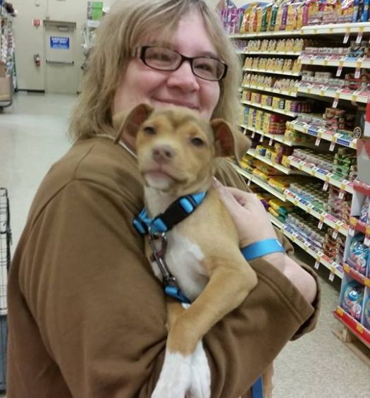 A woman holding a dog in a grocery store.