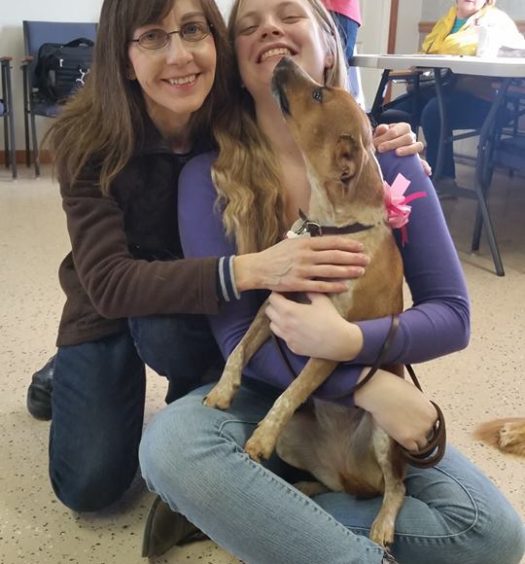 Two women hugging a dog in a room.