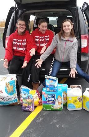 three teens siting on the trunk of their car showing products