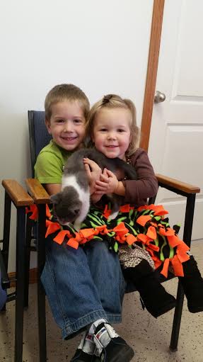 Two children sitting in a chair holding a cat.