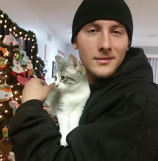 A man holding a cat in front of a christmas tree.