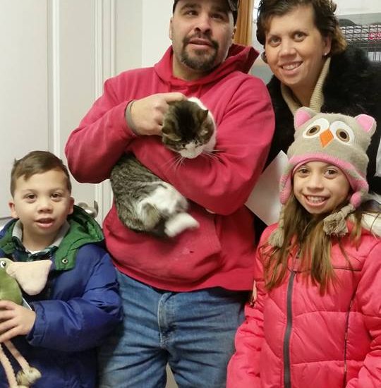 A family holding a cat in front of a door.