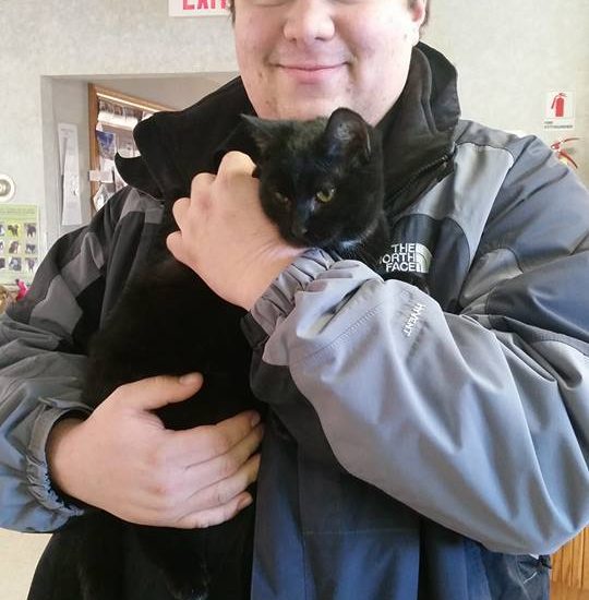 A young man holding a black cat.