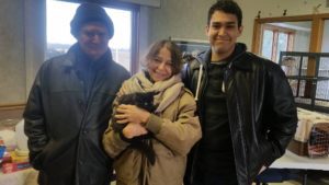 Three people holding a black cat in a room.