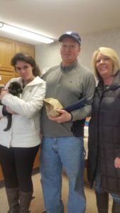 Three people standing in a room with a cat.