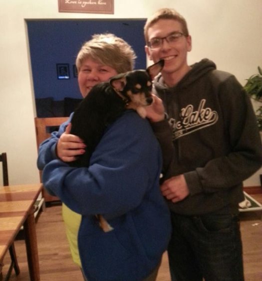 Two people standing next to a dog in a living room.