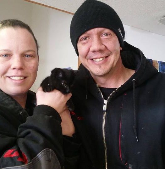 A man and woman smiling while holding a black kitten.