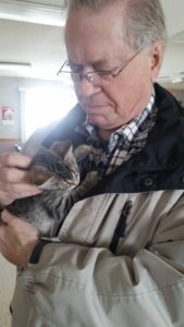 An older man holding a kitten in his arms.