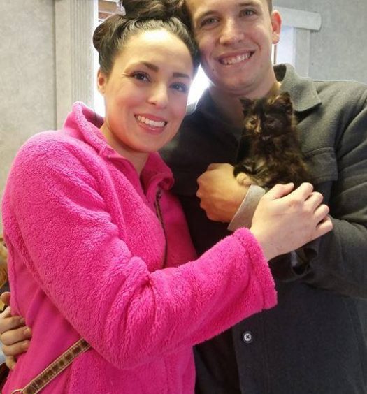 A man and woman posing for a picture holding a cat.
