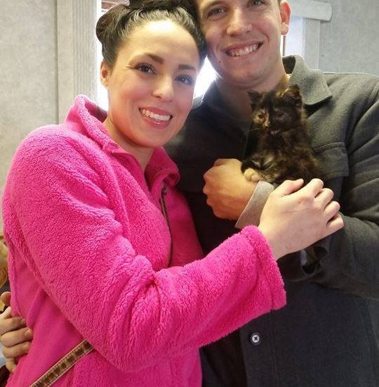 A man and woman posing for a picture holding a cat.