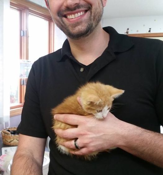A man holding an orange kitten in his arms.