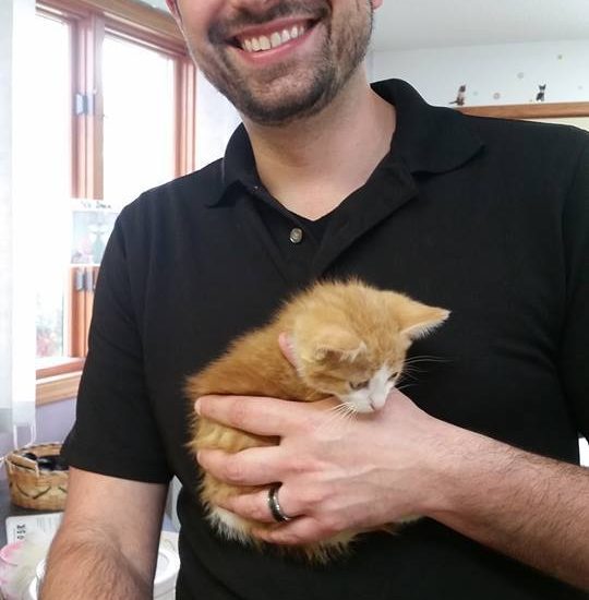 A man holding an orange kitten in his arms.