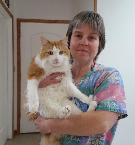 A woman holding an orange and white cat in a room.