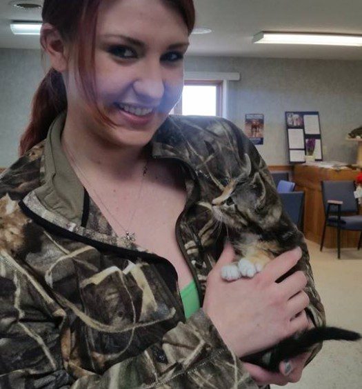 A woman in a camouflage jacket holding a kitten.