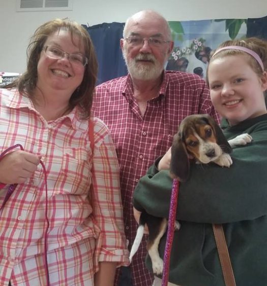 Two women and a man are posing for a picture with a beagle puppy.