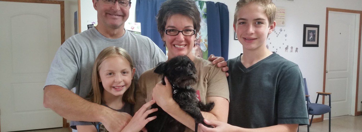 A family is posing for a picture with a black dog.