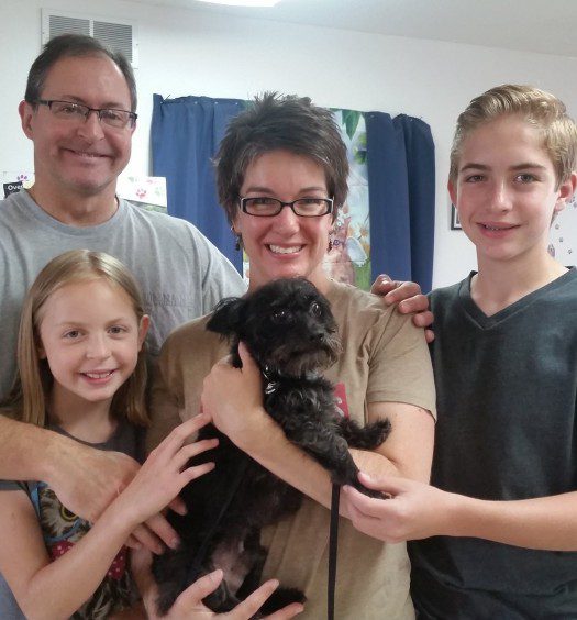 A family is posing for a picture with a black dog.