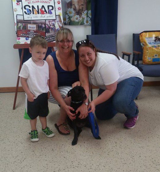 A woman and two children pose with a black dog.