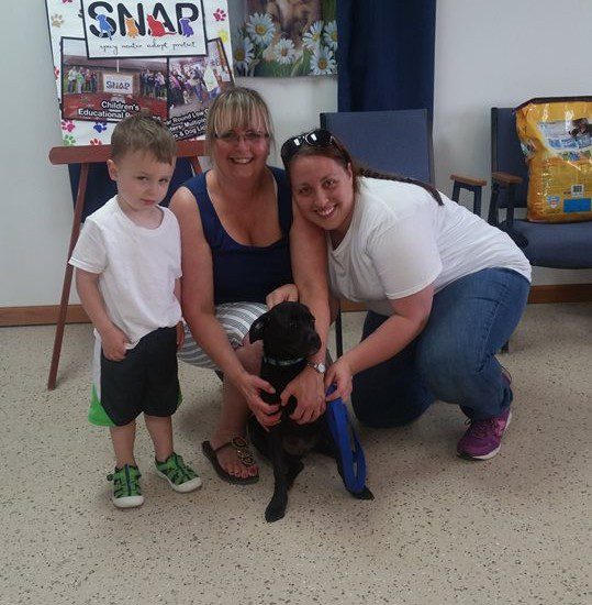 A woman and two children pose with a black dog.