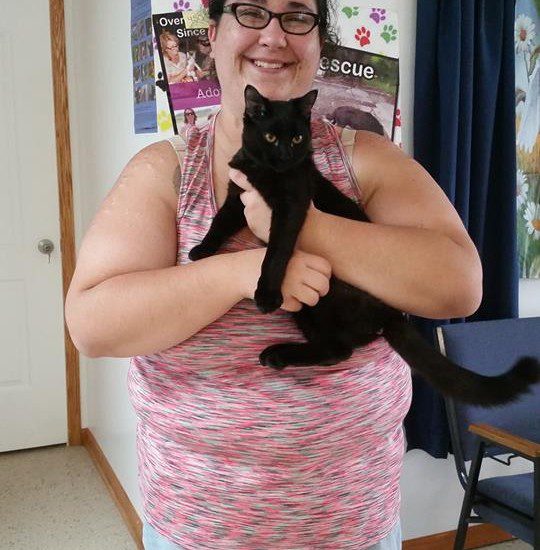 A woman holding a black cat in a room.