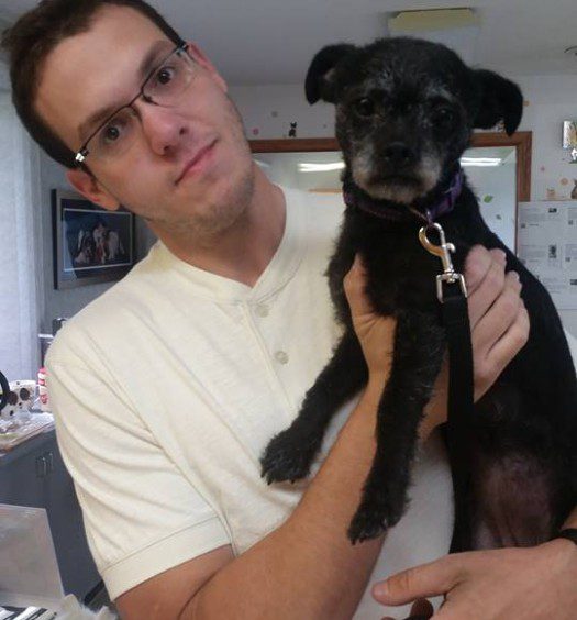 A man holding a small black dog in front of a counter.