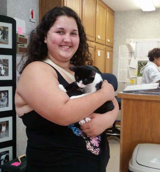 A woman holding a black and white cat in a kitchen.