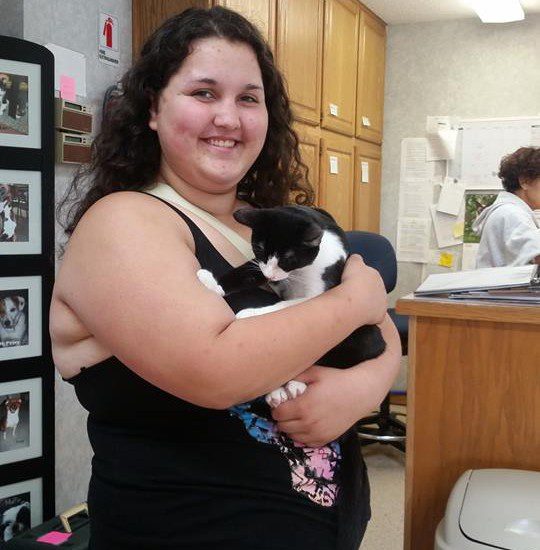 A woman holding a black and white cat in a kitchen.