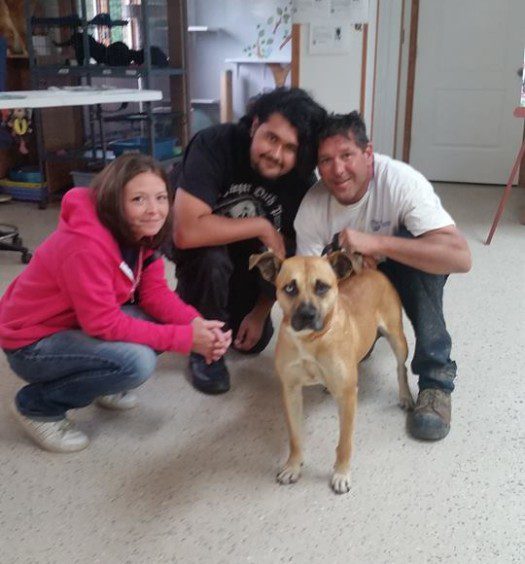 Three people posing with a dog in a room.