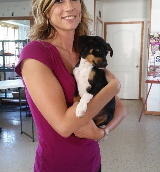 A woman holding a black and tan puppy in a room.