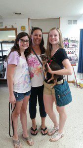 Three girls standing in a room with a dog.