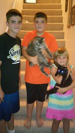 Three children standing on the stairs holding a black cat.