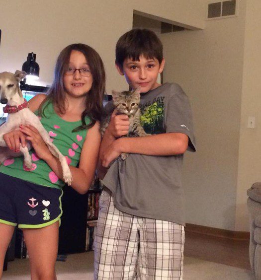 Two kids holding a cat and a dog in a living room.