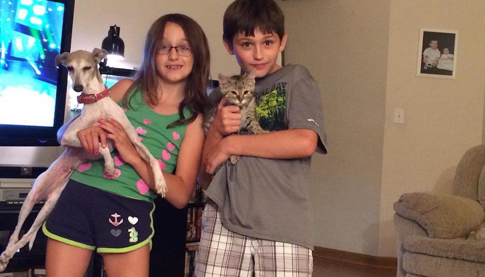 Two kids holding a cat and a dog in a living room.