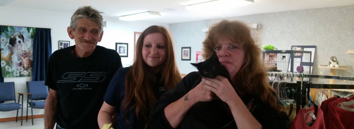 Three people standing next to a black cat in a clothing store.