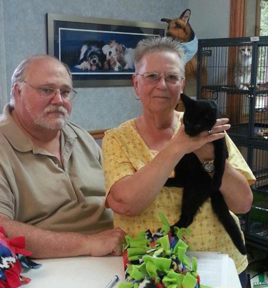 A man and woman holding a black cat at a table.