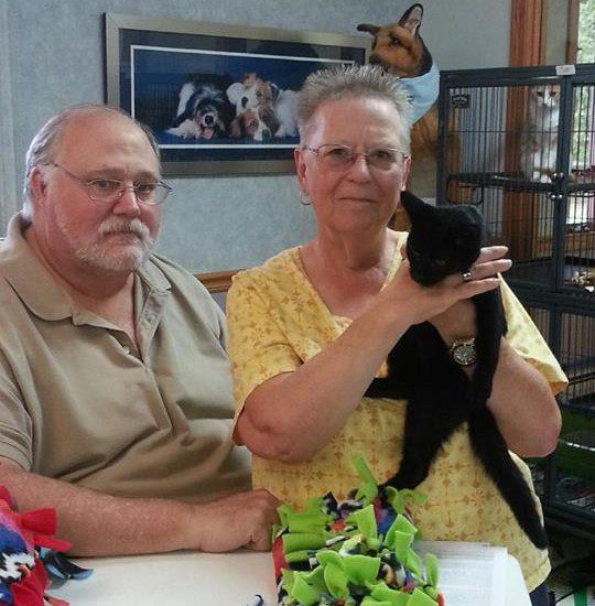 A man and woman holding a black cat at a table.