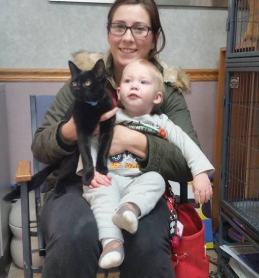 A woman sitting in a chair holding a black cat and a baby.