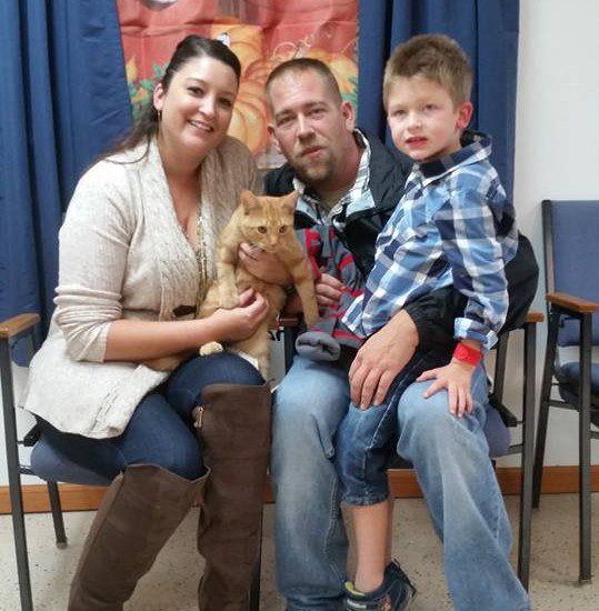 A man and woman pose with a cat in a waiting room.