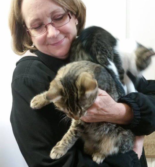 A woman is holding two cats in her arms.