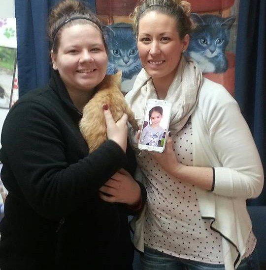 Two women posing for a picture with a cat.